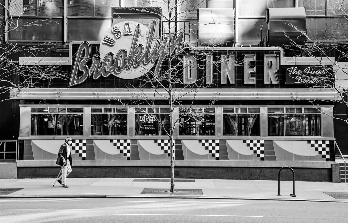 Schwarz-Weiß-Foto des Brooklyn Diner in New York City mit Neonreklamen und einem Fußgänger, der am Eingang vorbeigeht.