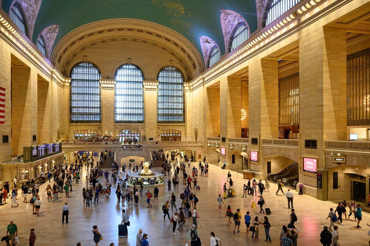 Weitwinkelansicht der Haupthalle des Grand Central Terminal, belebt von Menschen unter der gewölbten, mit Sternbildern dekorierten Decke und den großen Bogenfenstern.