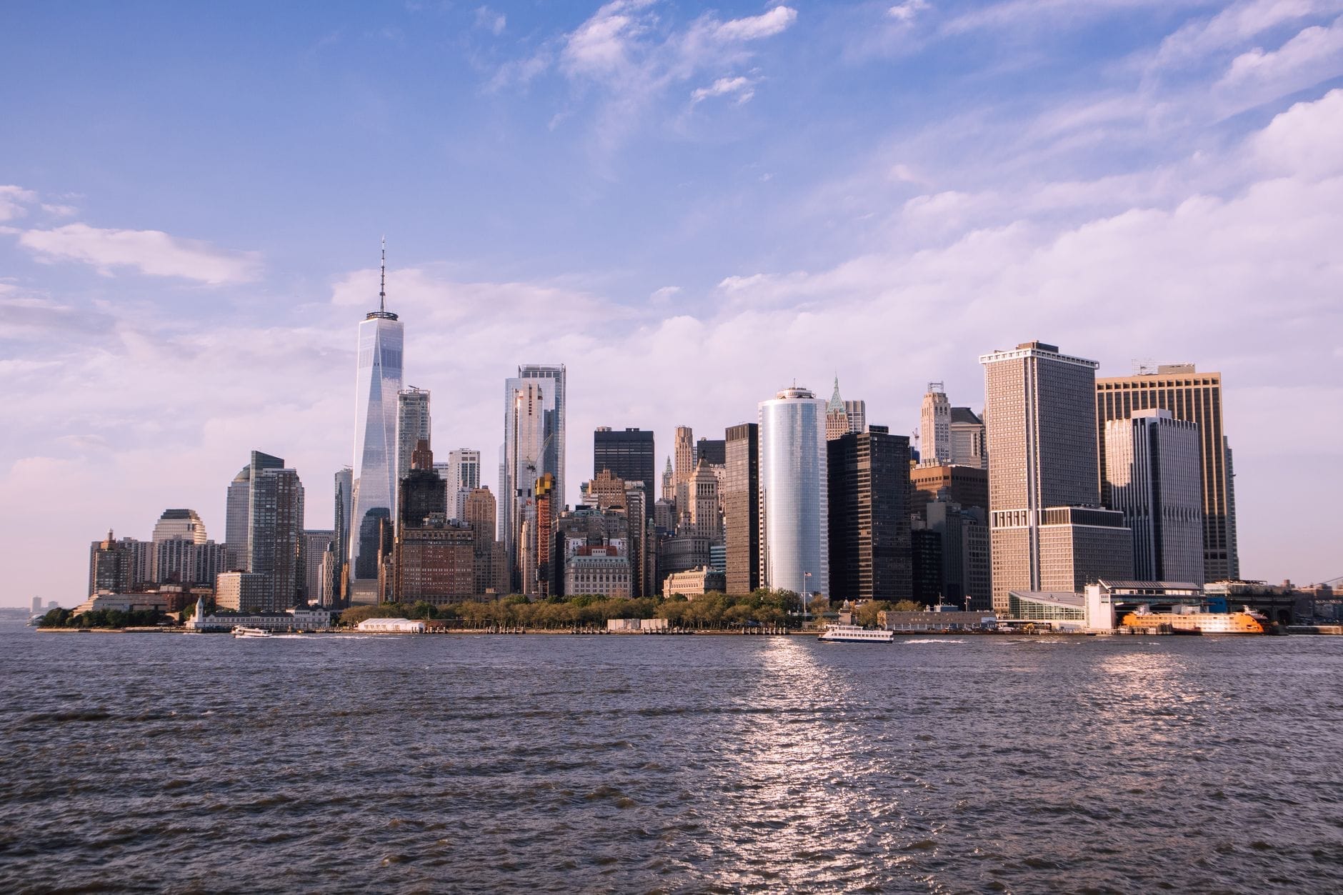 Vista panorâmica do skyline do Baixo Manhattan em Nova York visto do outro lado do Rio Hudson, com céu limpo e luz do sol refletindo na água.