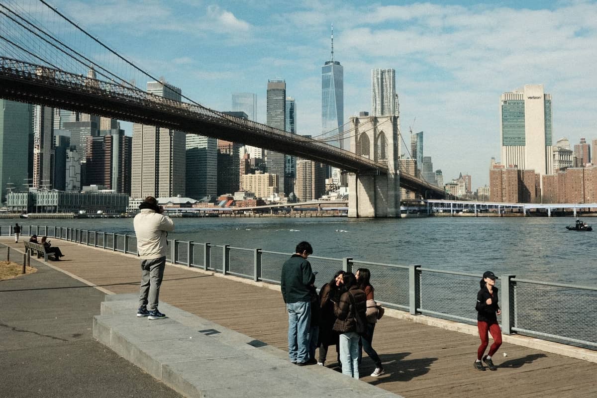 Blick auf die Brooklyn Bridge mit der Skyline von Manhattan, Familien und Kinder spazieren und machen Fotos entlang der Uferpromenade des East River.