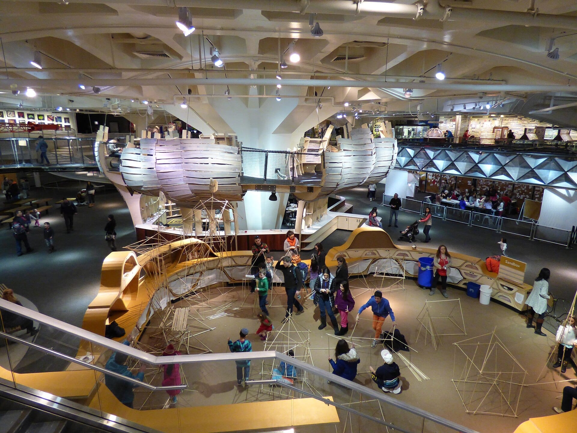 Vista interna del New York Hall of Science, con esposizioni interattive, strutture in legno e visitatori che esplorano l'ampia e moderna sala.