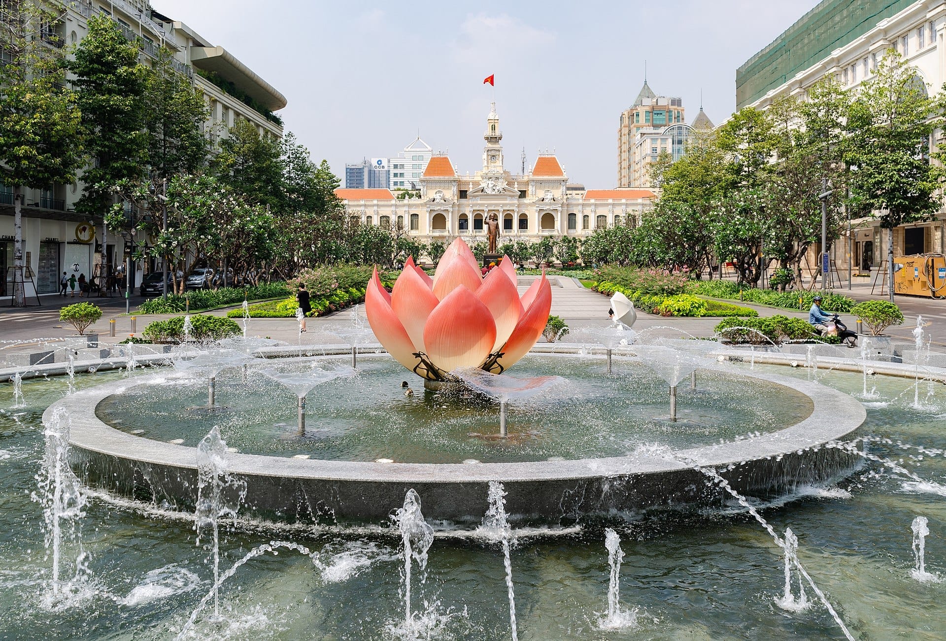 Gran fuente de loto rosa rodeada de chorros de agua en el centro de la calle peatonal Nguyễn Huệ, con el Edificio del Comité Popular al fondo.