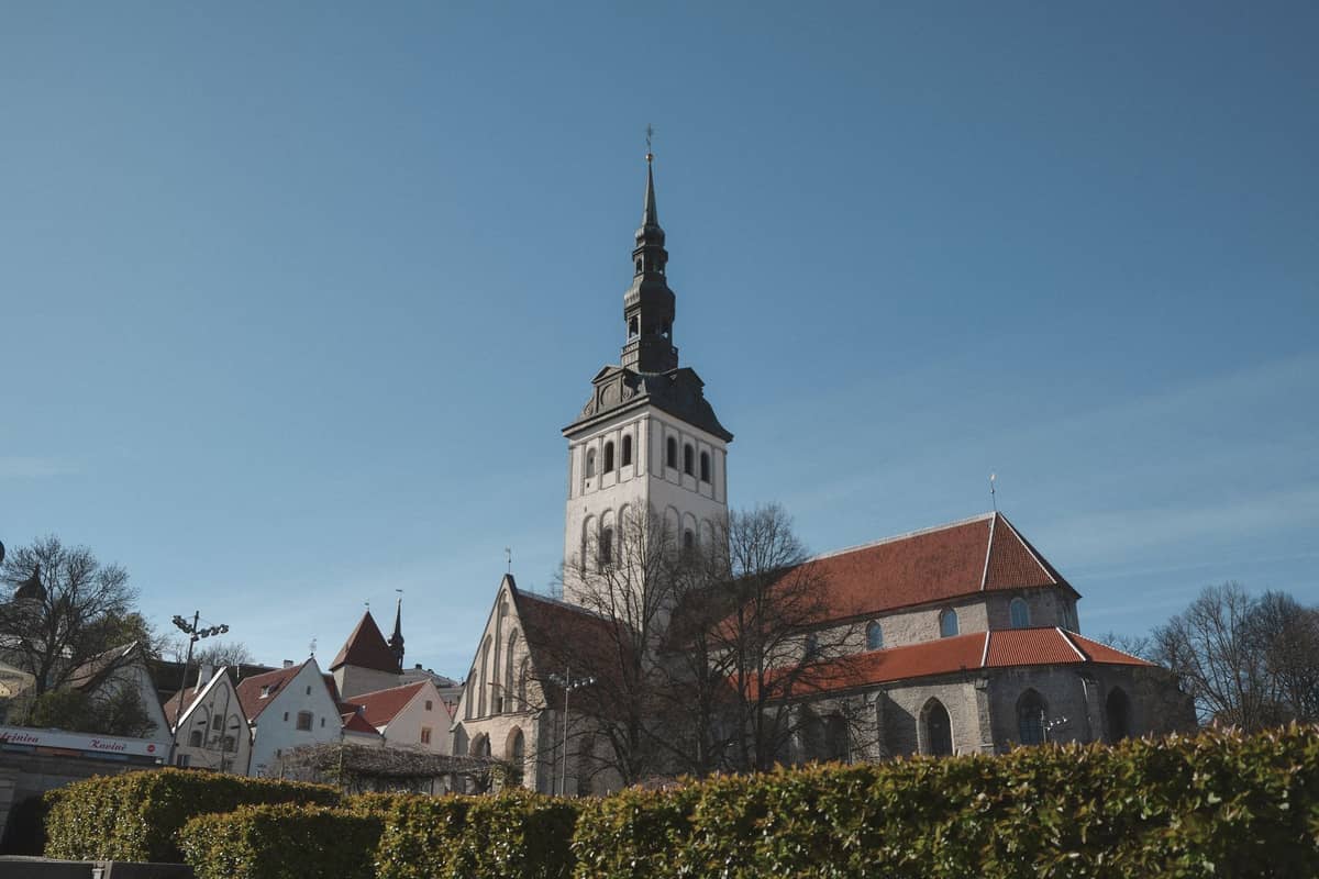 Außenansicht des Niguliste Museums – eine restaurierte gotische Kirche mit hohem Turm und rotem Ziegeldach in Tallinns Altstadt unter strahlend blauem Himmel.