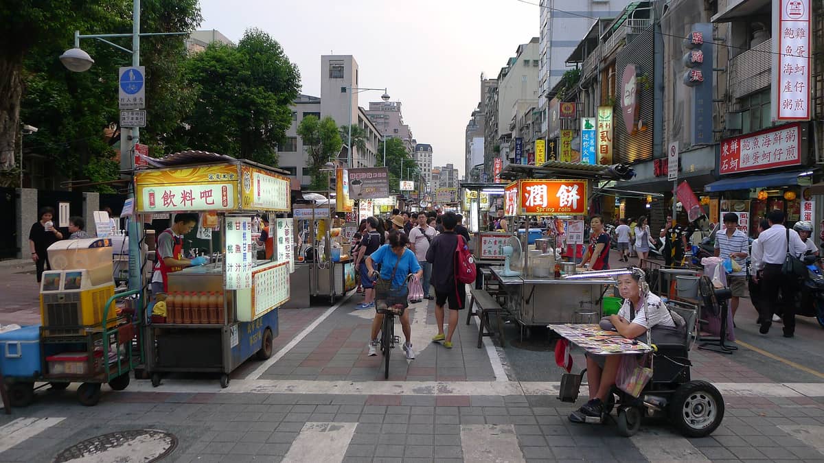 Ein belebter Fußgängerabschnitt des Ningxia Nachtmarkts in Taipei, gesäumt von Essensständen und Schildern, mit zahlreichen Besuchern am Abend.