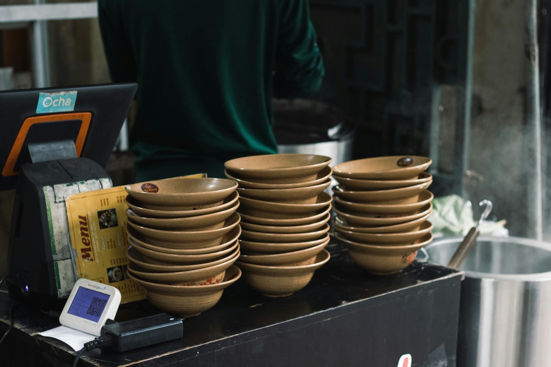 Stack of ceramic bowls on a counter in a casual restaurant with a menu and cash register visible.