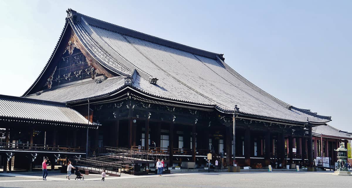 Wide view of the grand main hall at Nishi Hongan-ji Temple in Kyoto, showcasing its large traditional roof, wooden architecture, and spacious courtyard.