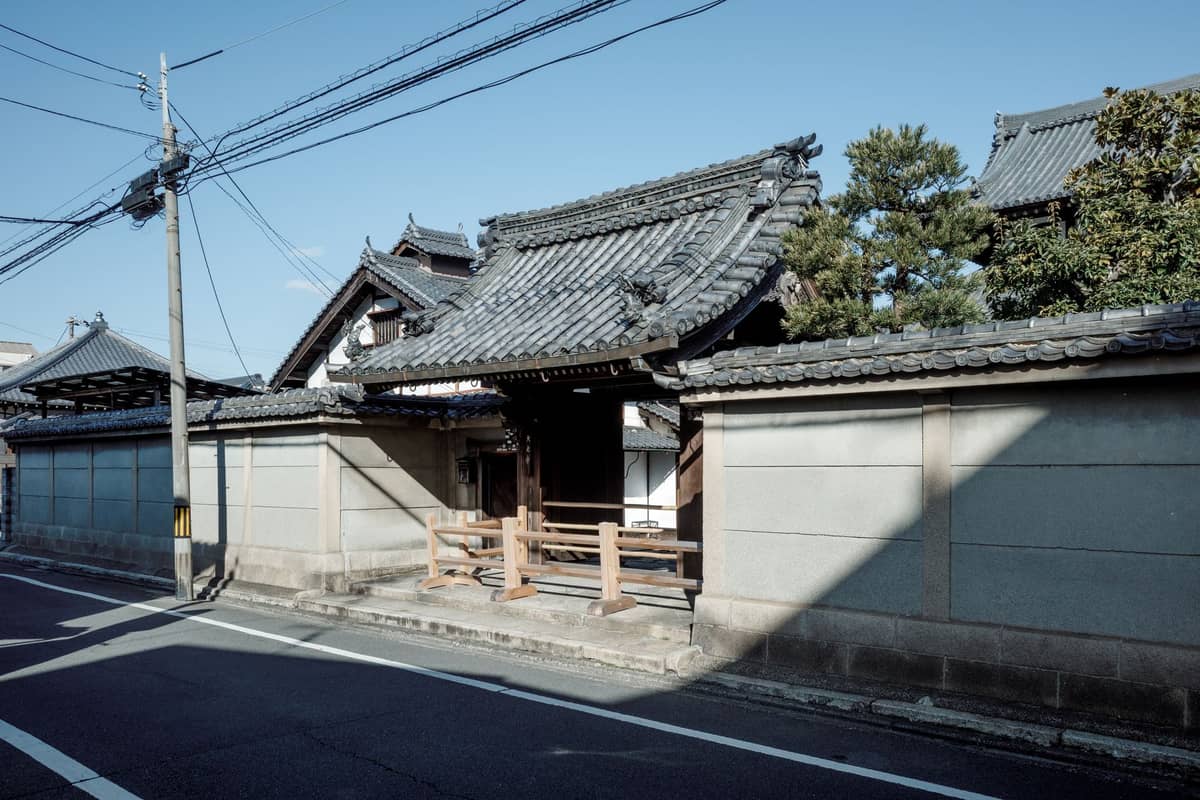 Street view in Nishijin, Kyoto showing a traditional Japanese tiled gate and wooden buildings representative of the district's historic fabric.