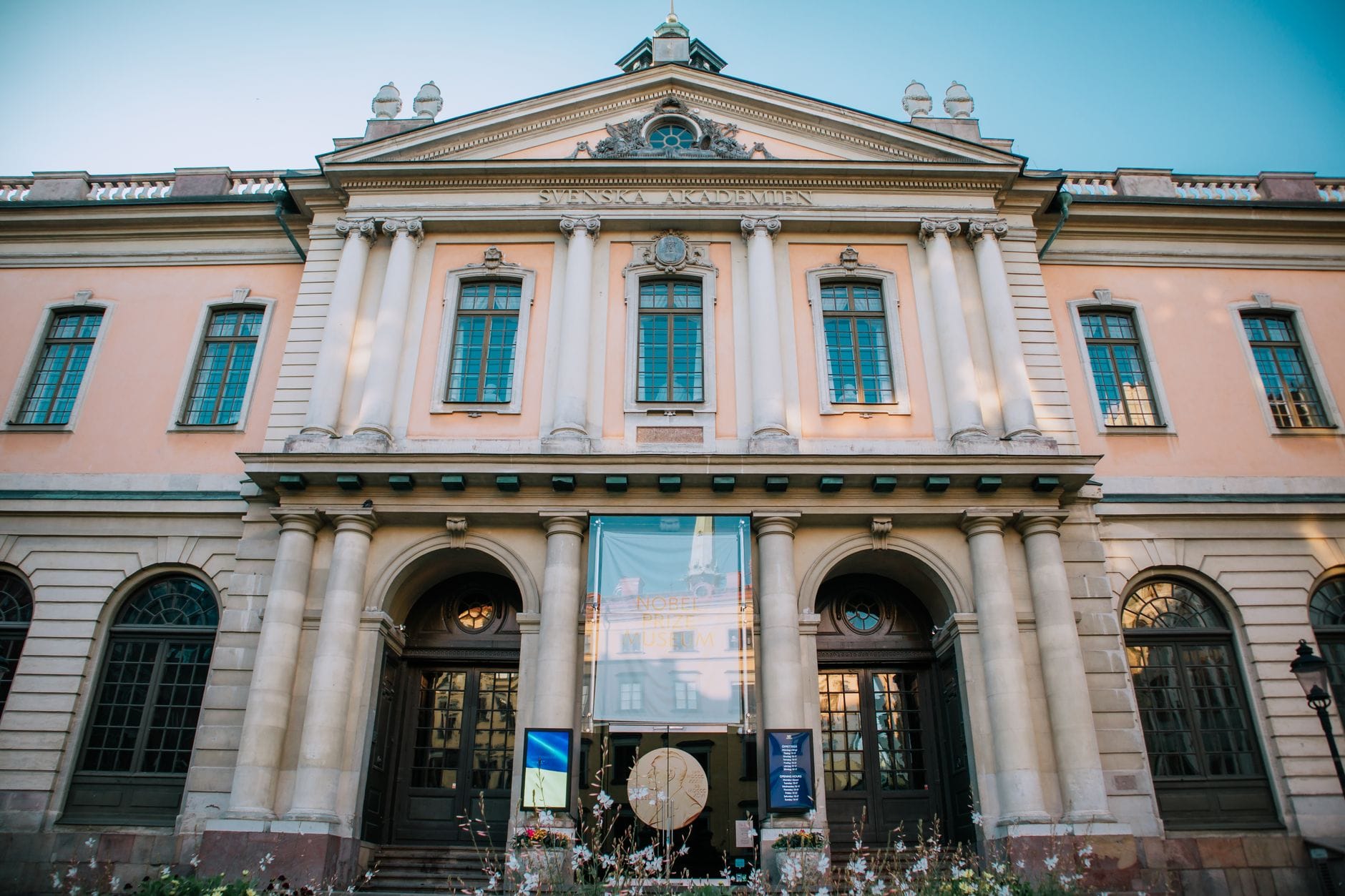 ด้านหน้าของอาคาร Nobel Museum ในสตอกโฮล์มที่มีสถาปัตยกรรมนีโอคลาสสิกและหน้าต่างบานใหญ่ ถ่ายในเวลากลางวัน