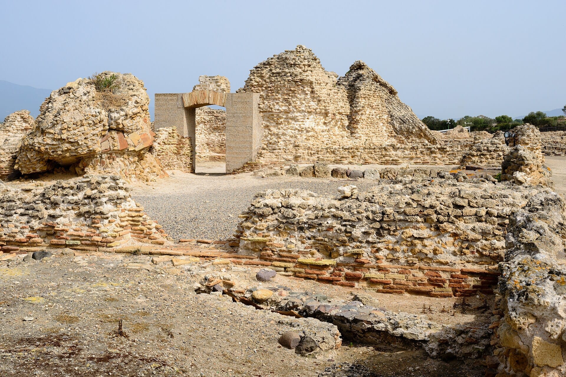 Alte Steinruinen und Ziegelmauern an der archäologischen Stätte Nora auf Sardinien unter einem klaren blauen Himmel.