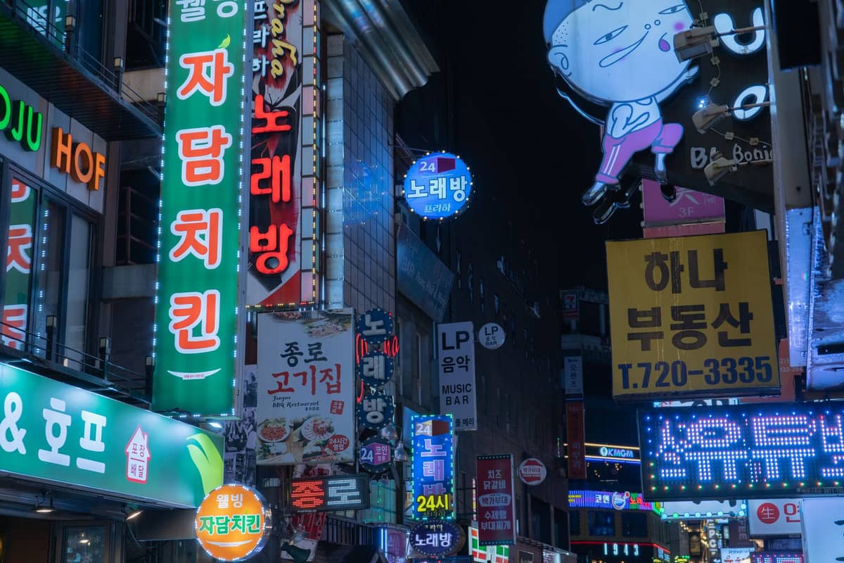 Uma cena de rua colorida à noite em Seoul com muitas placas de néon, incluindo algumas de locais de karaokê noraebang.
