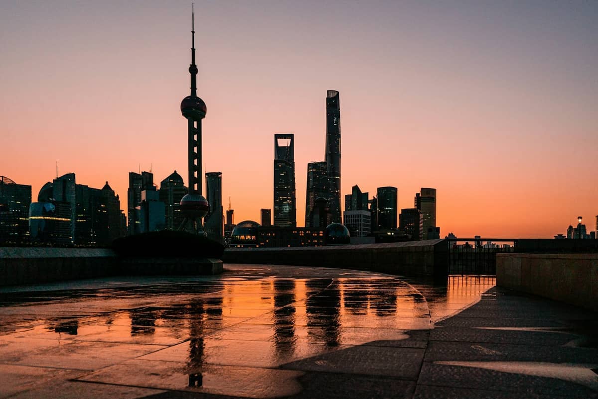 Blick auf die Pudong-Skyline von Shanghai bei Sonnenuntergang vom North Bund Riverside, mit nassen Promenadenfliesen, die den orangefarbenen Abendhimmel widerspiegeln.