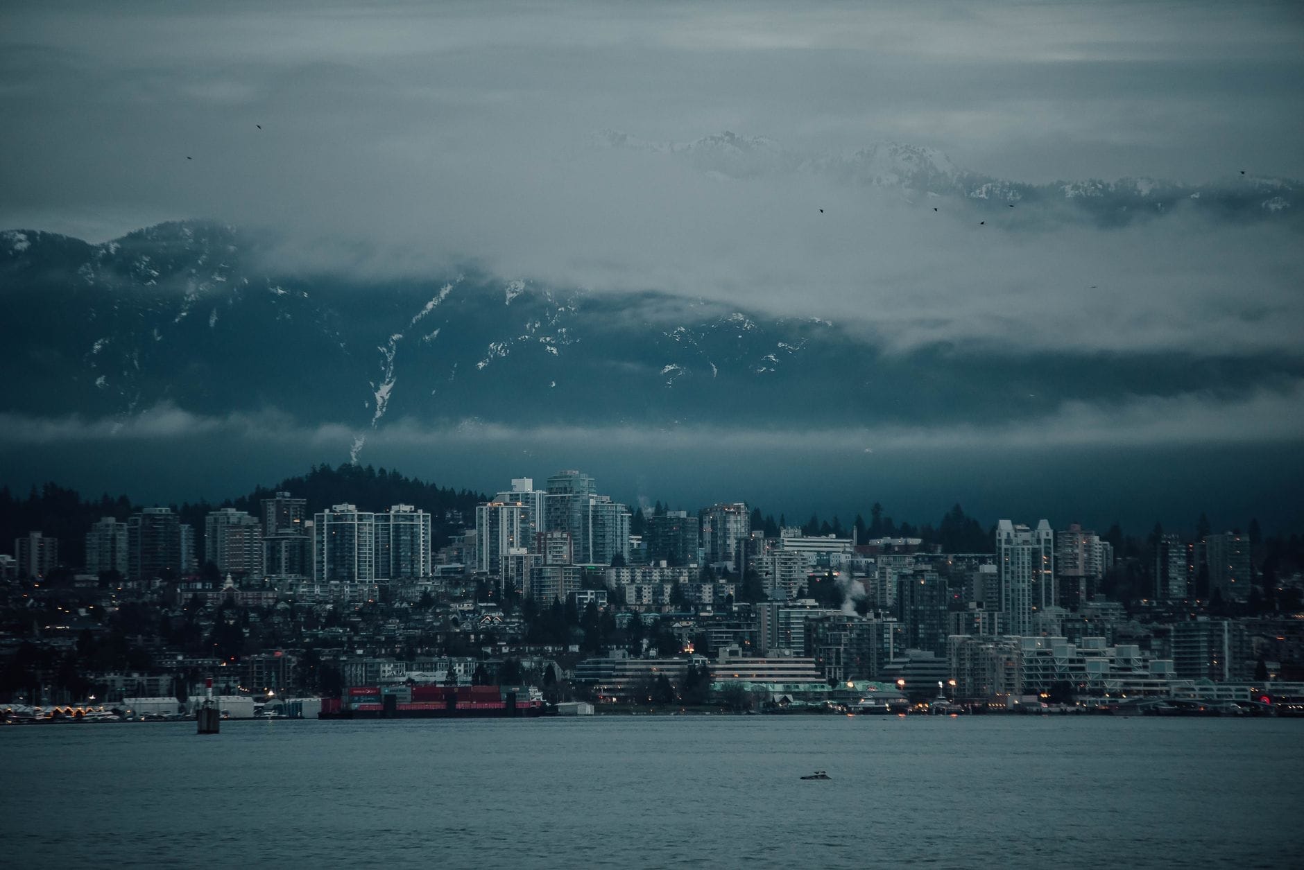 วิวเมือง North Vancouver กับฉากหลังเป็นภูเขาสูงตระหง่าน มีเมฆจับยอดเขาและ Burrard Inlet อยู่ข้างหน้า แสงบรรยากาศหม่นอมเทา