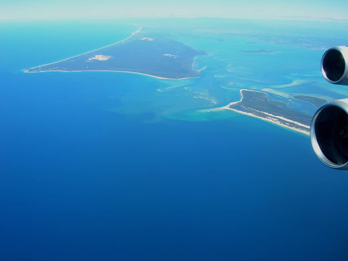 Luftaufnahme von North Stradbroke Island, umgeben vom blauen Ozean und einer sandigen Küstenlinie, fotografiert durch ein Flugzeugfenster.