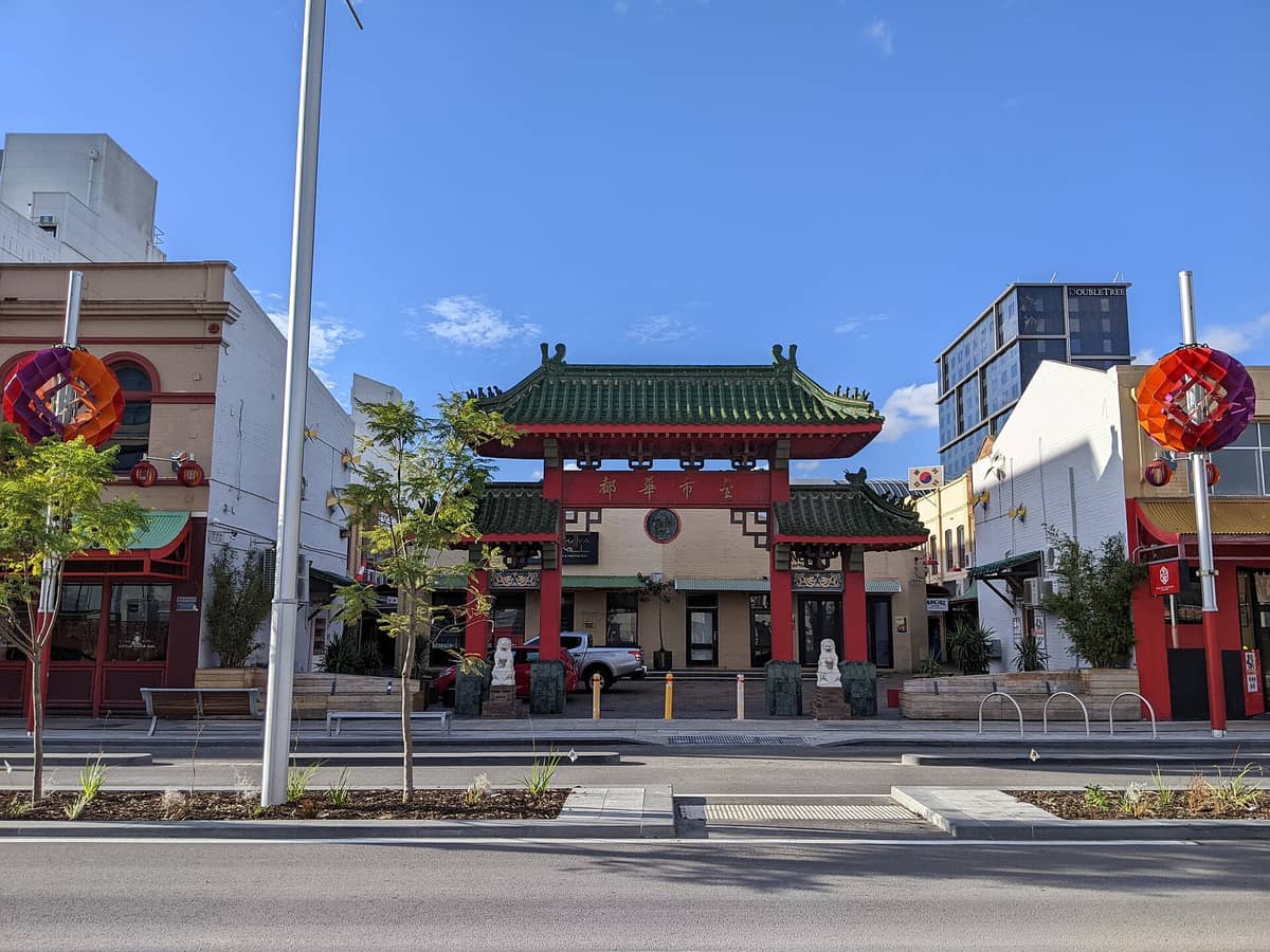 Główna chińska brama Chinatown w Northbridge, Perth, widziana od strony ulicy Roe Street z charakterystycznymi czerwonymi kolumnami, zielonym dachówkowym dachem i rzeźbami latarni po bokach.