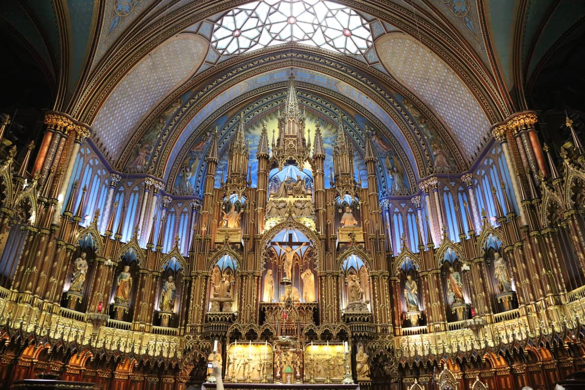 Der reich verzierte Altar und das indigoblaue Gewölbe der Basilique Notre-Dame de Montréal mit goldenen Details, Statuen und Buntglasfenstern.