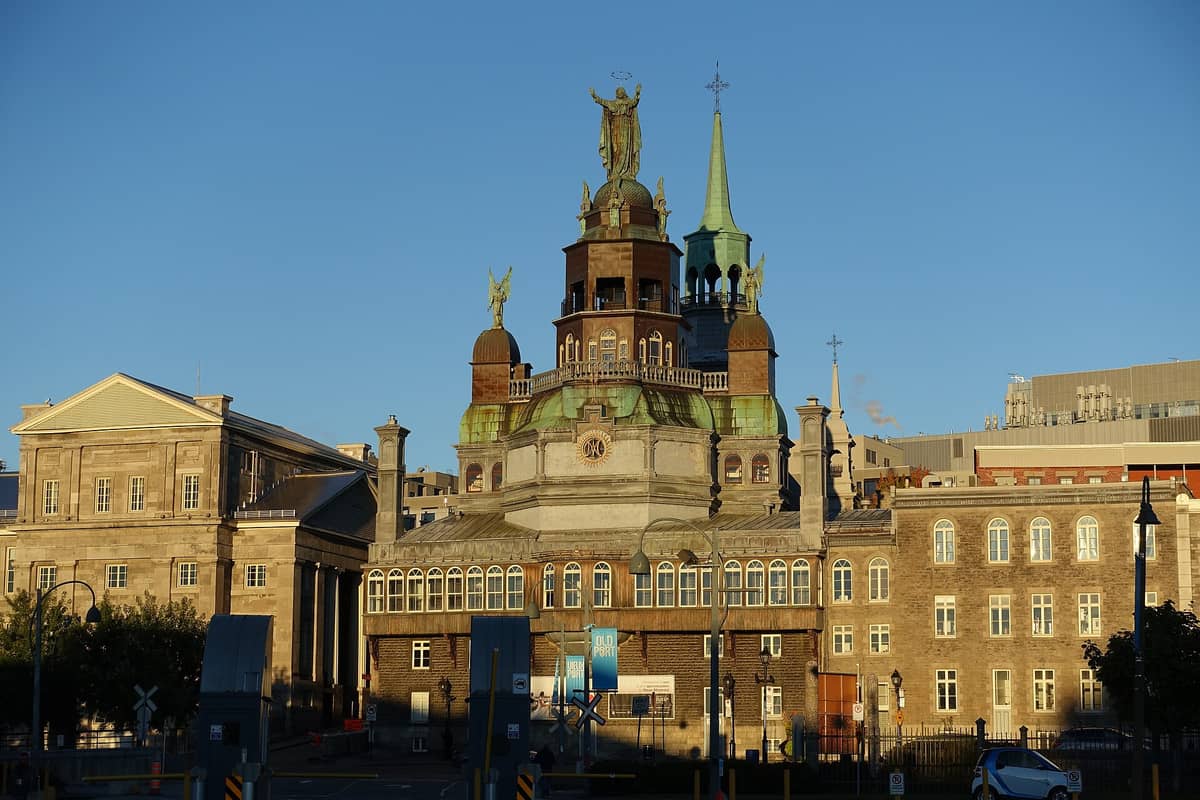 Weitwinklige Außenansicht der Notre-Dame-de-Bon-Secours-Kapelle in Montréal mit ihren markanten grünen Kupferskulpturen und Glockentürmen vor strahlend blauem Himmel.