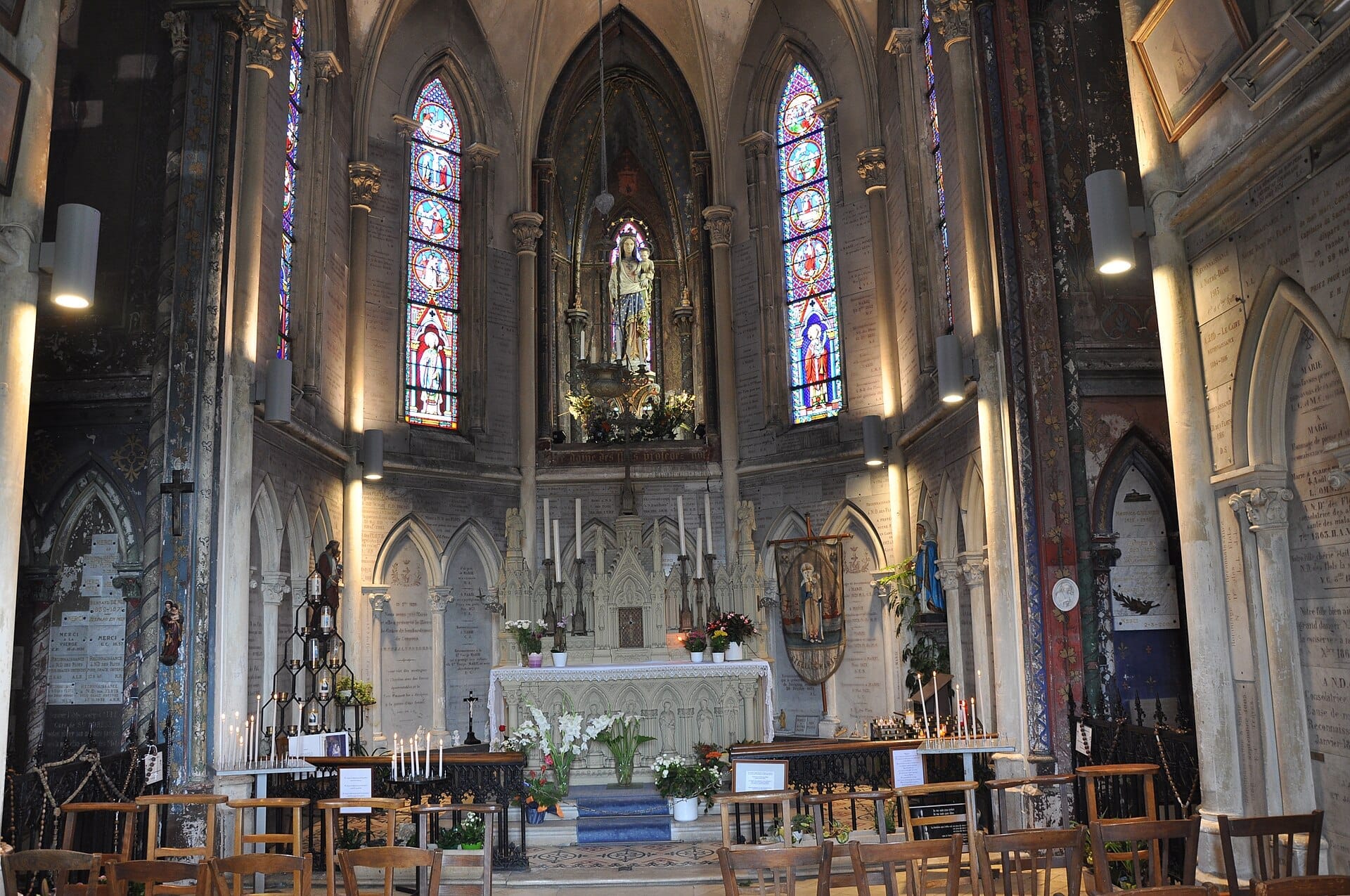 ภายในของ Chapelle Notre-Dame-des-Flots ที่มีสถาปัตยกรรมนีโอโกธิคอันวิจิตร หน้าต่างกระจกสี เก้าอี้ไม้ และเทียนจุดไฟจำนวนมากใกล้แท่นบูชา