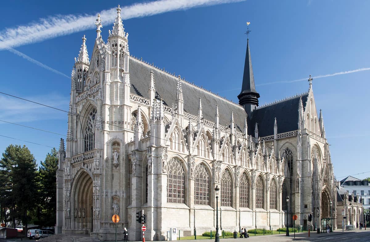 Vista externa ampla da Igreja Notre-Dame du Sablon em Bruxelas, exibindo em detalhes a arquitetura gótica brabantina sob um céu azul.