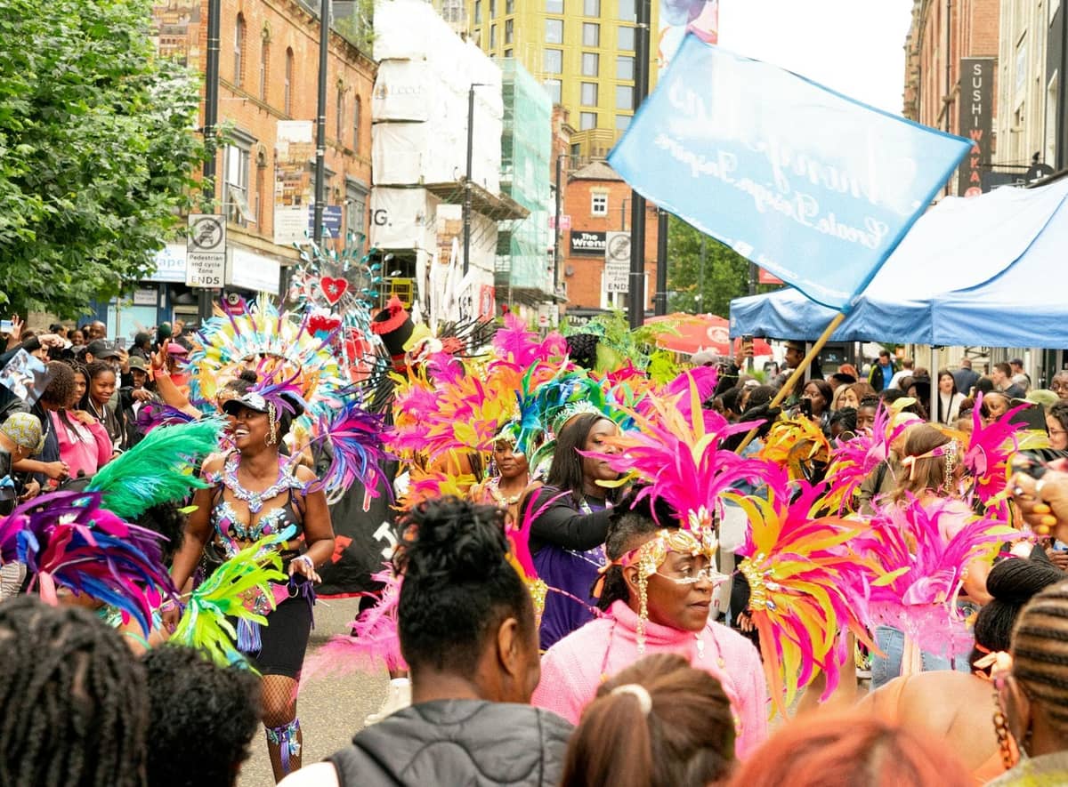 Performers de desfile com fantasias coloridas e multidões comemorando ao ar livre em uma rua de Londres durante um festival vibrante.