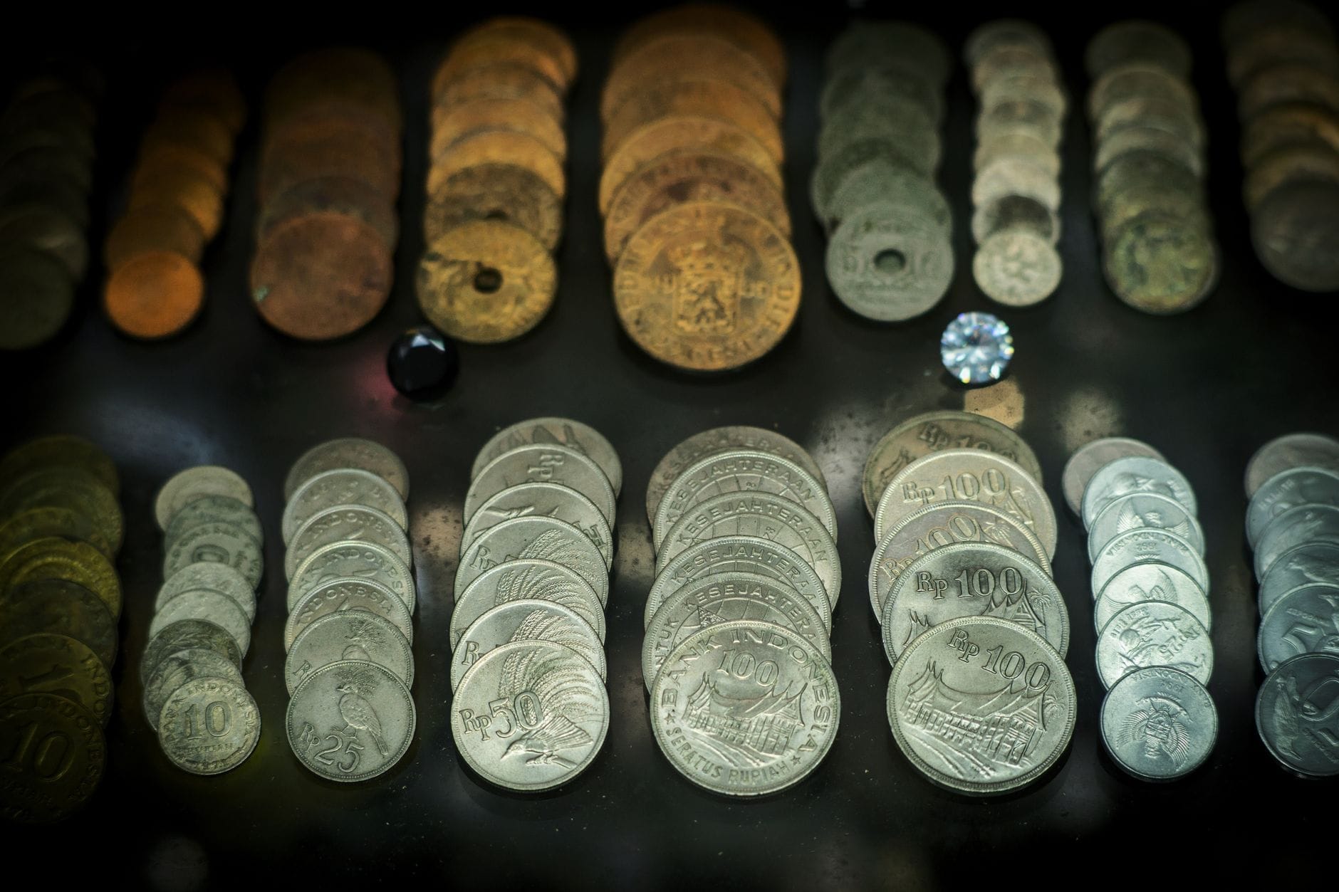 File di monete antiche e moderne esposte in una teca museale su sfondo scuro, a testimonianza della varietà e della storia della valuta ad Atene.