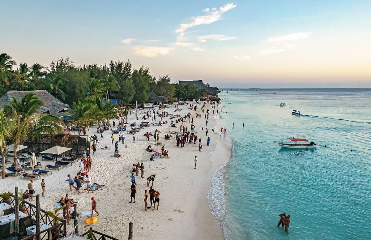 ชายหาดนุงวีช่วงพระอาทิตย์ตกเต็มไปด้วยผู้คน เพลิดเพลินกับทรายขาว น้ำทะเลใสต้นปาล์ม และอาคารหลังคามุงจากริมฝั่ง