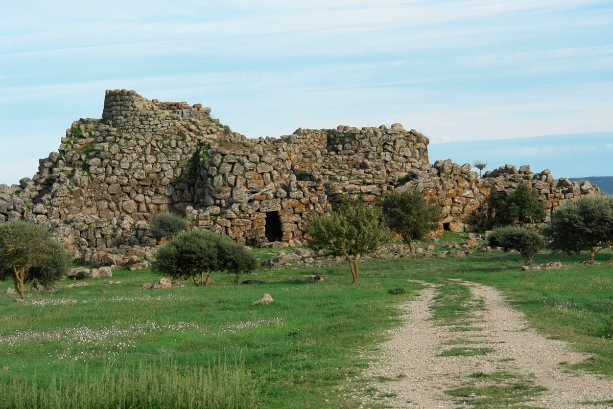 Nuraghe Arrubiu, eine mächtige antike Steinfestung, erhebt sich inmitten von grünem Gras und vereinzelten Sträuchern unter einem blauen Himmel in der Nähe von Orroli, Sardinien.