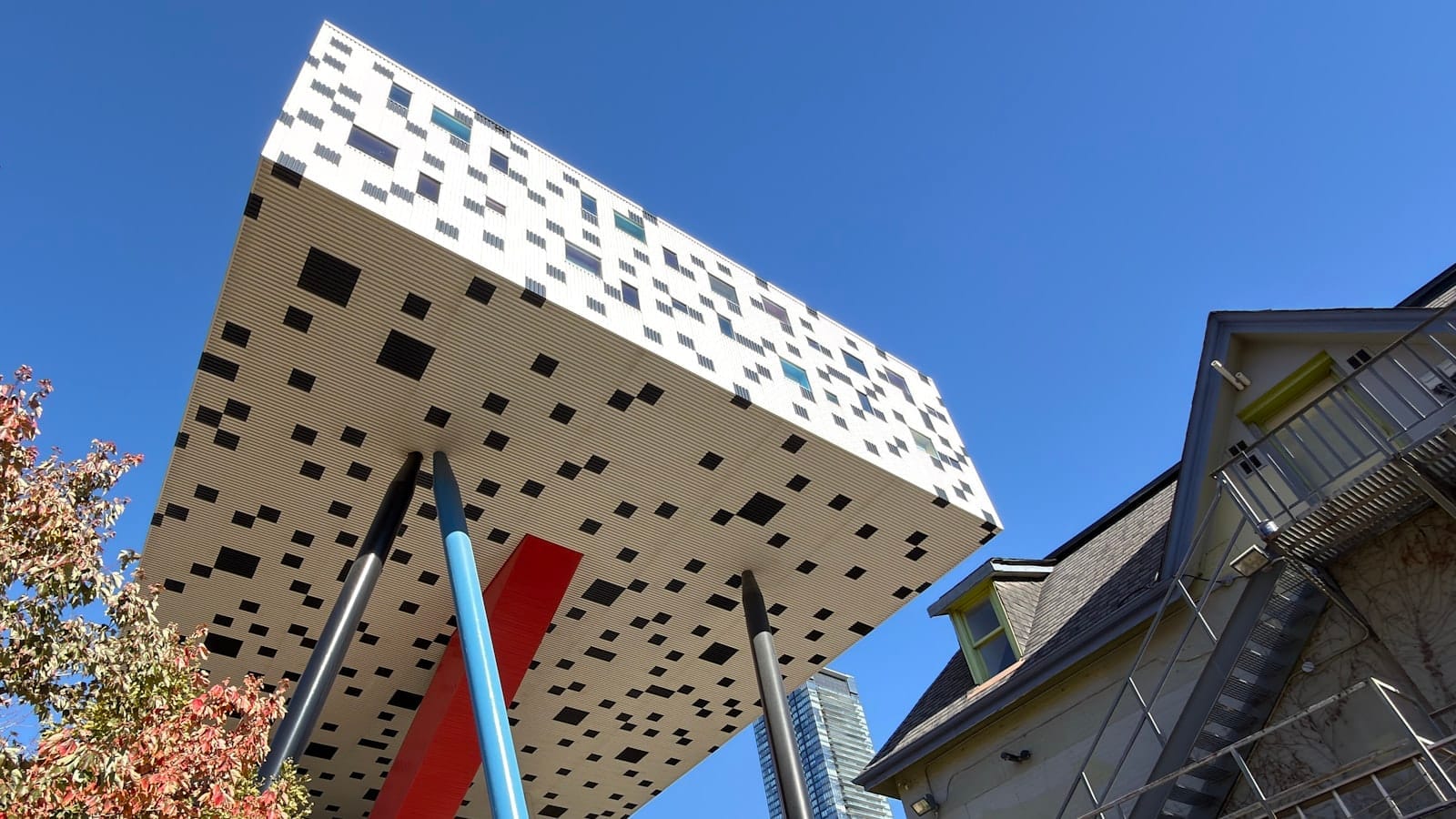 อาคาร Sharp Centre for Design ของ OCAD University ที่มีกล่องสีขาวดำแบบพิกเซลยกสูงบนเสาสีสันสดใสที่เอียงทำมุม ตัดกับท้องฟ้าสีฟ้าใส
