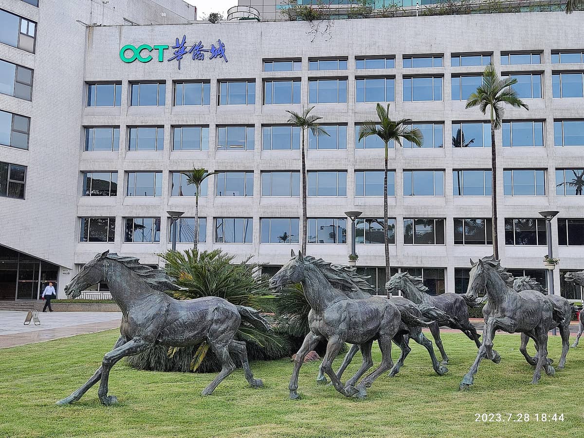 Esculturas de bronze de cavalos em corrida em frente ao edifício principal com a sigla 'OCT' e letreiros em chinês na Overseas Chinese Town, em Nanshan, Shenzhen.