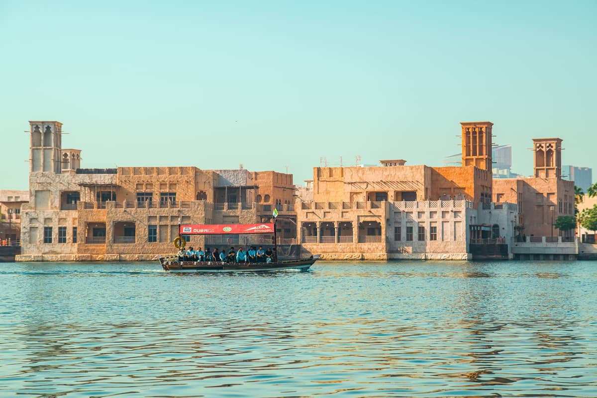 Traditionelle Windturm-Gebäude und ein Abra-Boot überqueren den Dubai Creek – historische Architektur und Alltagsleben im Creek-Viertel von Alt-Dubai.
