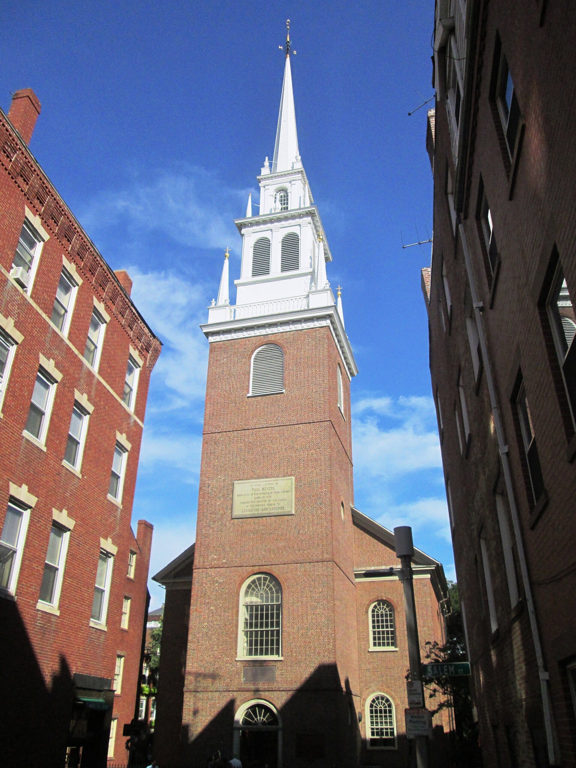 La facciata in mattoni e l'alto campanile bianco della Old North Church si ergono tra storici edifici in mattoni rossi sotto un cielo azzurro limpido a Boston.