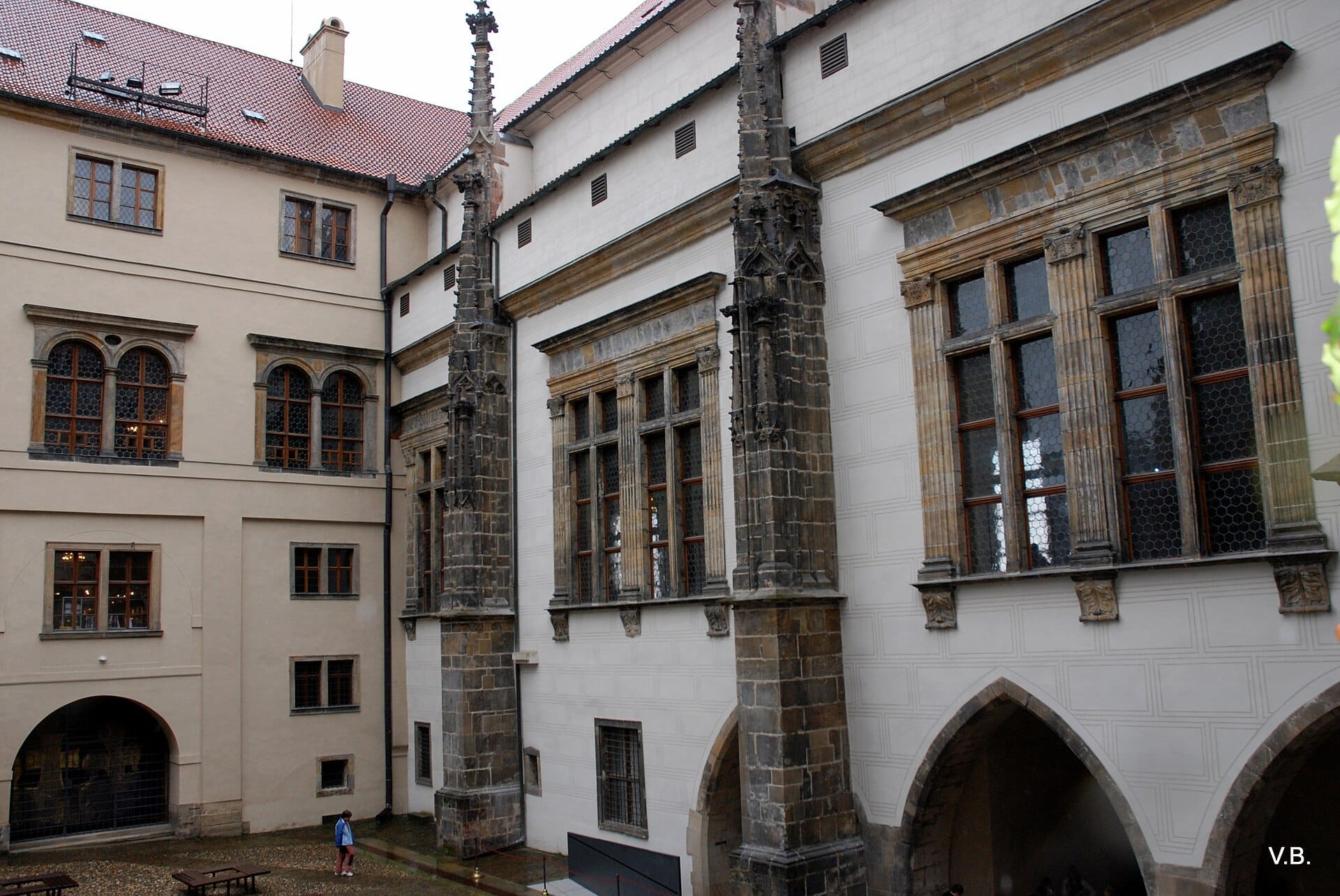 Außenansicht des Alten Königspalastes auf der Prager Burg mit Bogenfenstern, gotischen Türmen und Steinsäulen an einem bewölkten Tag.