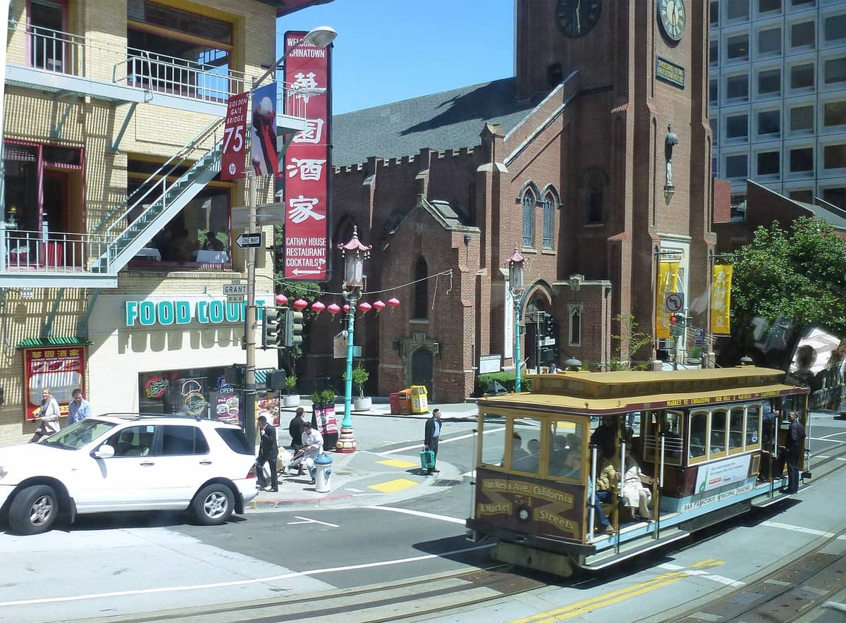 Vista desde la calle de la Antigua Catedral de Saint Mary en el Chinatown de San Francisco, con su característica fachada de ladrillo, la torre gótica y la animada escena callejera de Chinatown, incluido un teleférico.