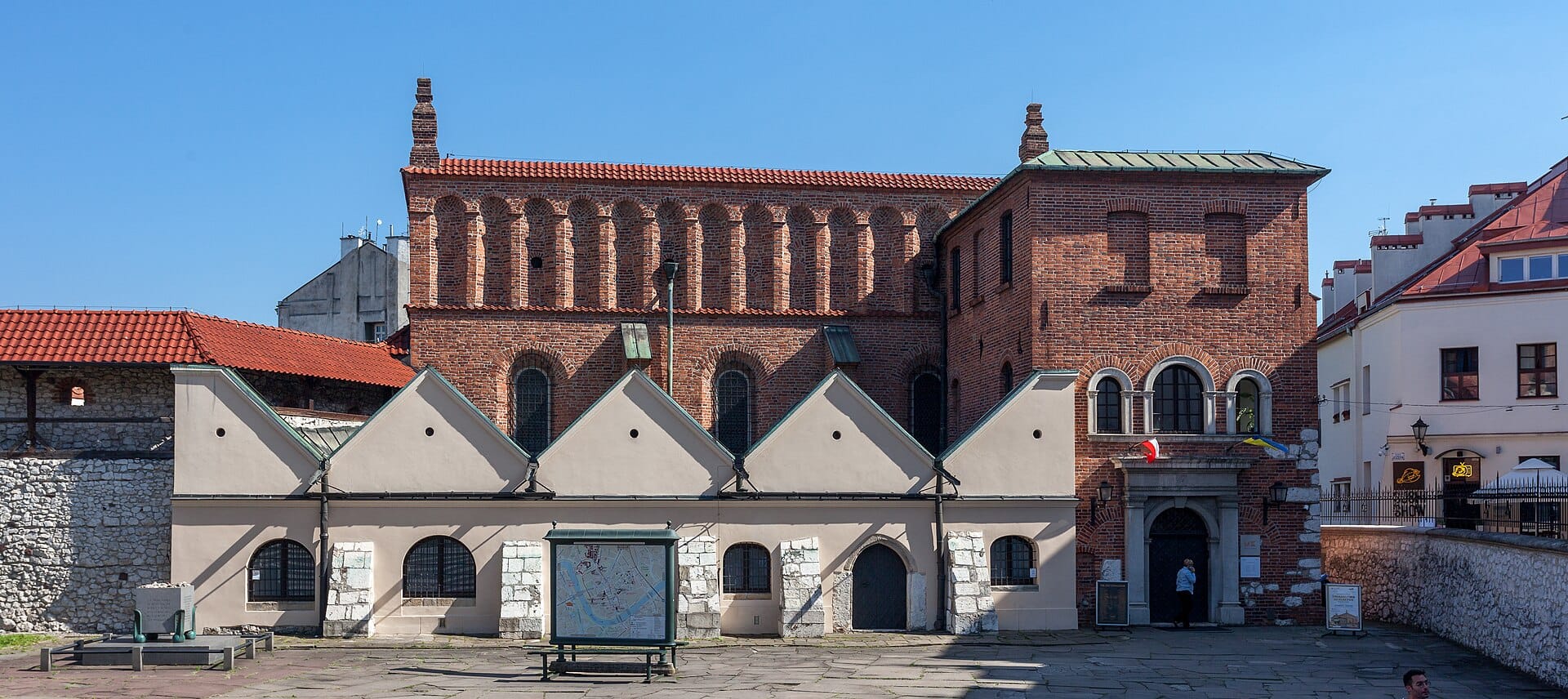 มุมมองกว้างของโบสถ์ยิวเก่า (Stara Synagoga) ในคราคูฟ เห็นตัวอาคารอิฐแดงกับหน้าต่างโค้งหลายบานใต้ท้องฟ้าสีฟ้าสดใส