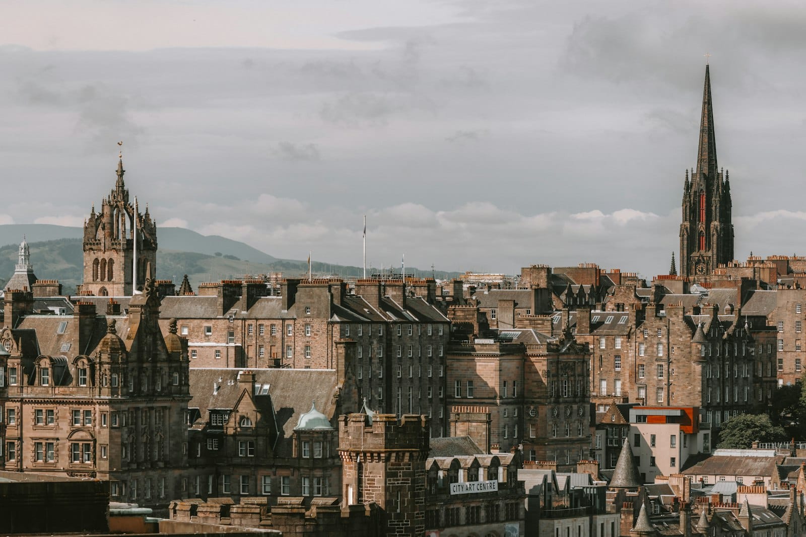 Skyline der Edinburgher Altstadt mit historischen Sandsteingebäuden und Kirchturmspitzen unter bewölktem Himmel – ein Blick auf die mittelalterliche Architektur und dichte Bebauung der Stadt.