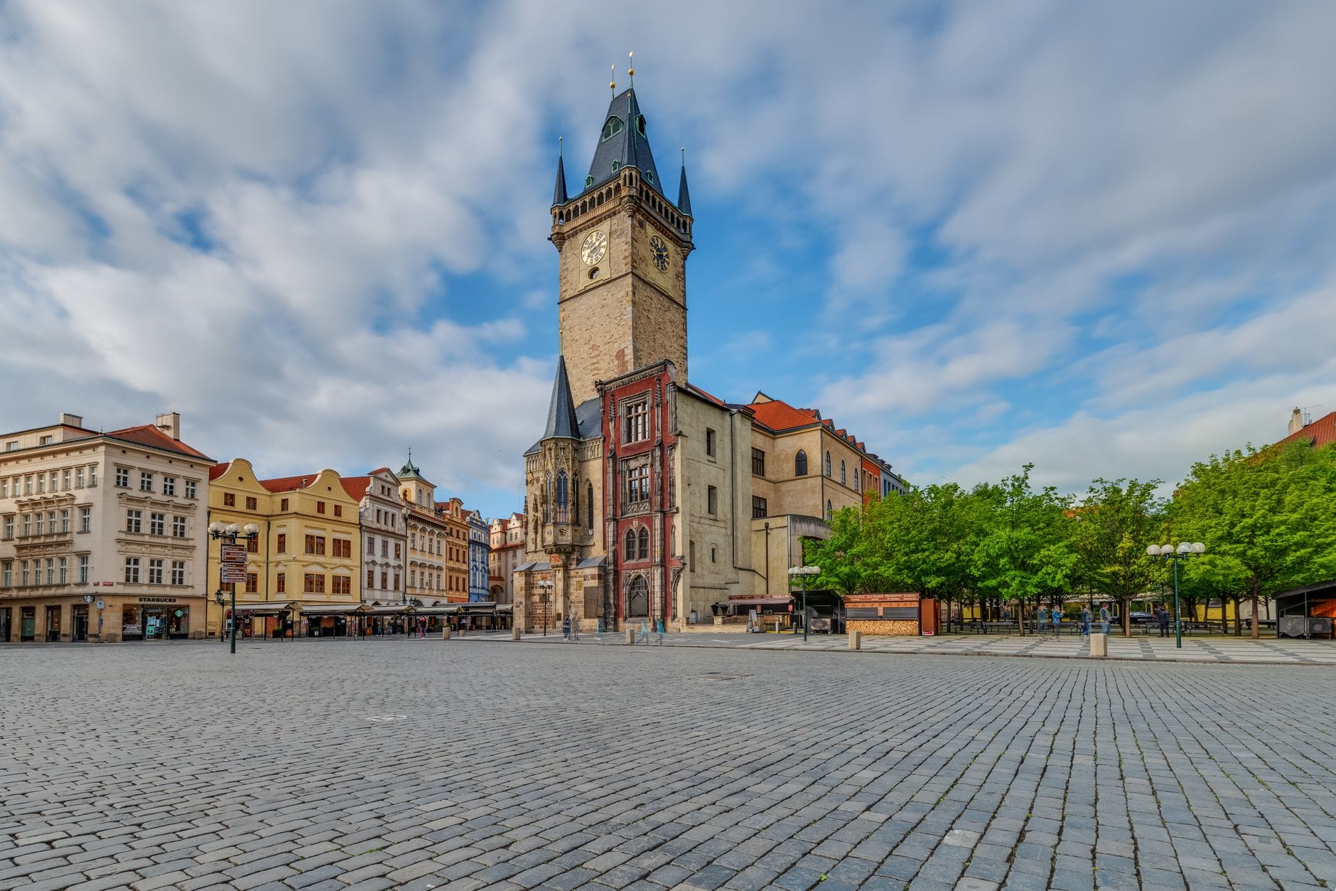 Vista grandangolare della Torre del Municipio della Città Vecchia che si innalza sulla Piazza della Città Vecchia di Praga, circondata da edifici storici sotto un cielo blu con qualche nuvola.