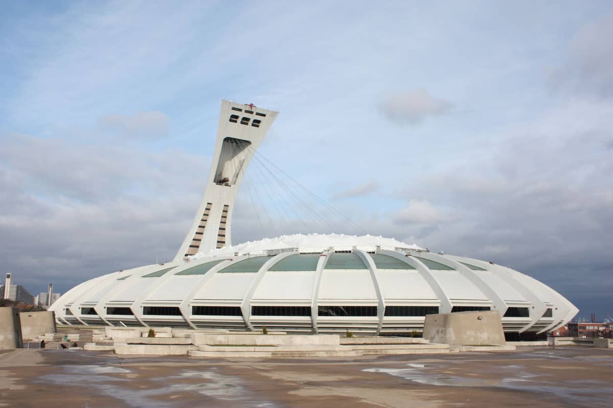 Weitwinkelperspektive auf das Olympiastadion Montréal mit dem ikonischen geneigten Turm vor bewölktem Himmel, die gesamte Kuppelstruktur ist zu sehen.