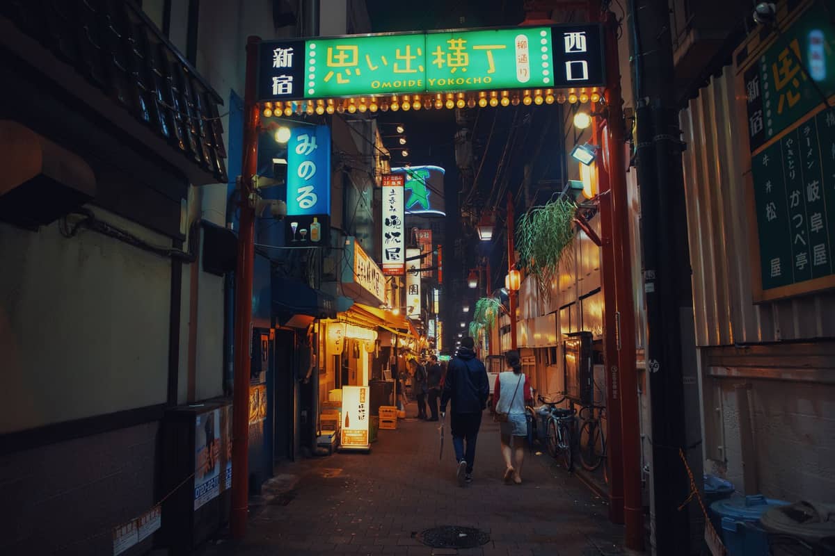 Night view of Omoide Yokocho entrance in Shinjuku with glowing signage, narrow alley, and people walking beneath the iconic neon-lit gate.