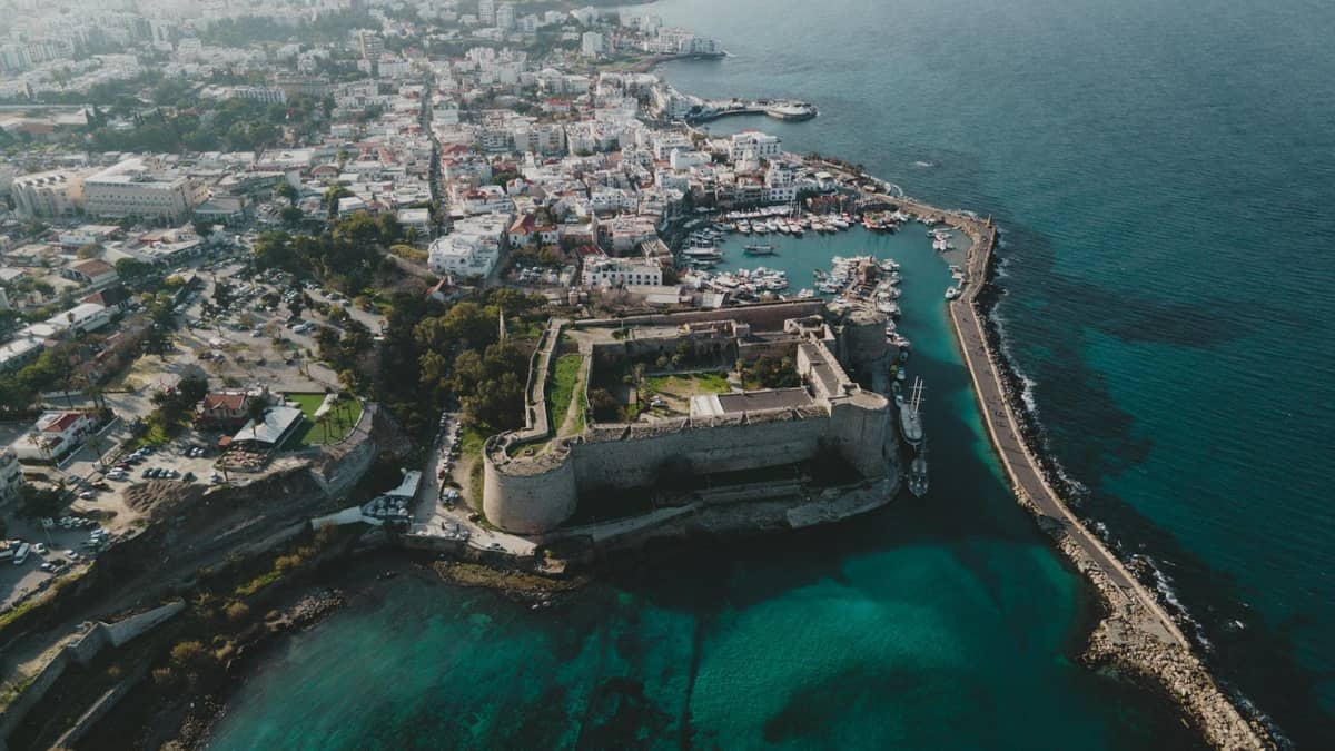Aerial view of Rethymno harbor with the large Venetian fortress surrounded by turquoise waters, city buildings, and a long sea wall.
