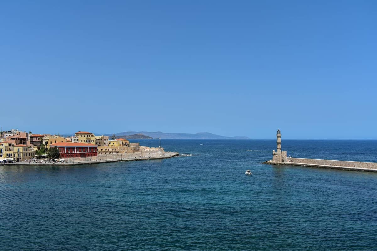 Chania's Venetian harbor with colorful waterfront buildings and iconic lighthouse under clear blue sky, Crete, Greece