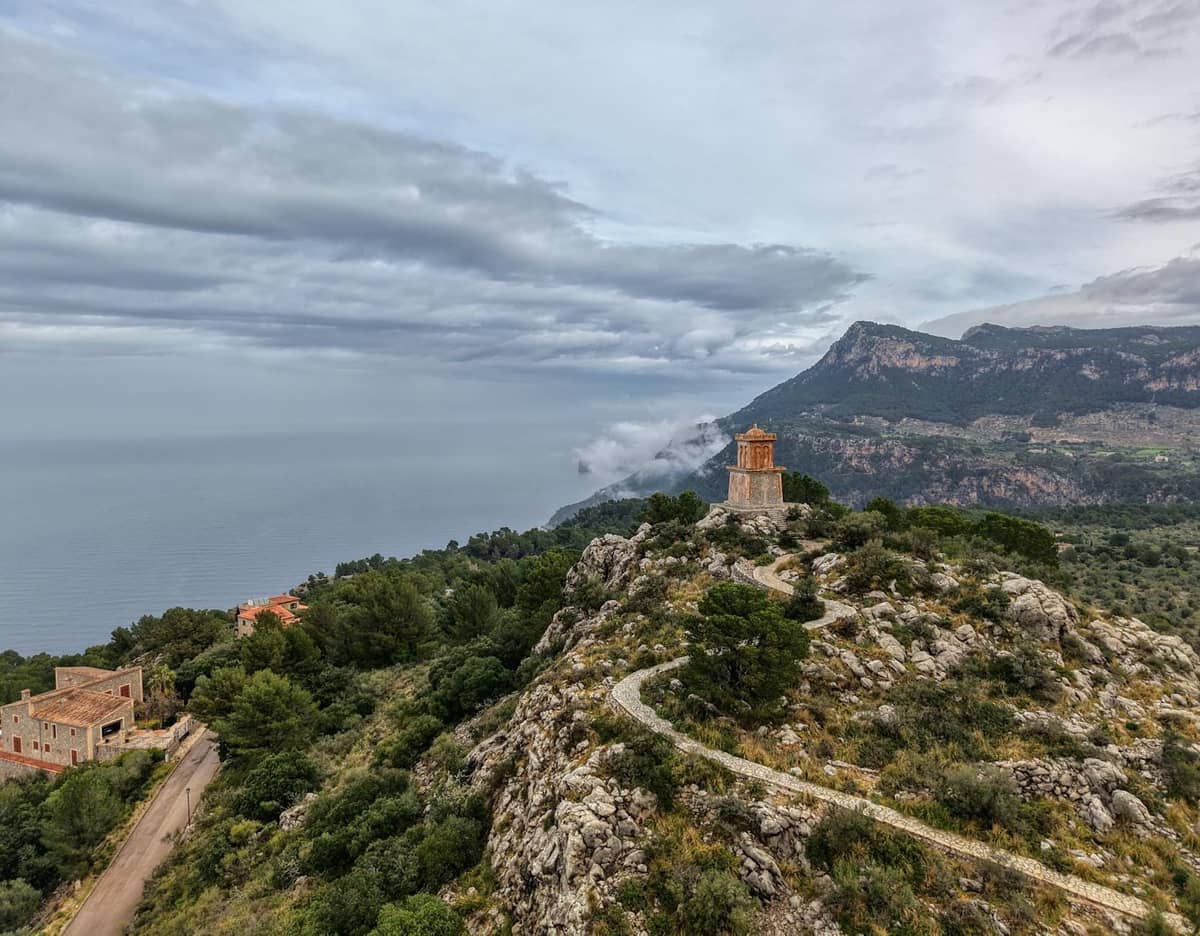 Edificio in pietra in cima a una collina con sentiero tortuoso, affacciato sulle aspre montagne e sul Mar Mediterraneo nella Serra de Tramuntana di Maiorca.