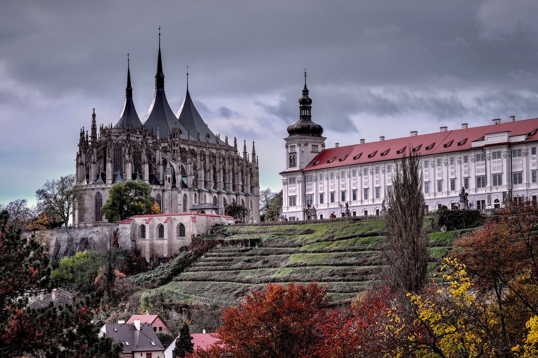 Dramatische Weitwinkelansicht der gotischen St.-Barbara-Kathedrale und des angrenzenden Jesuitenkollegs in Kutná Hora mit Blick auf die terrassierte Hügelseite im Herbst