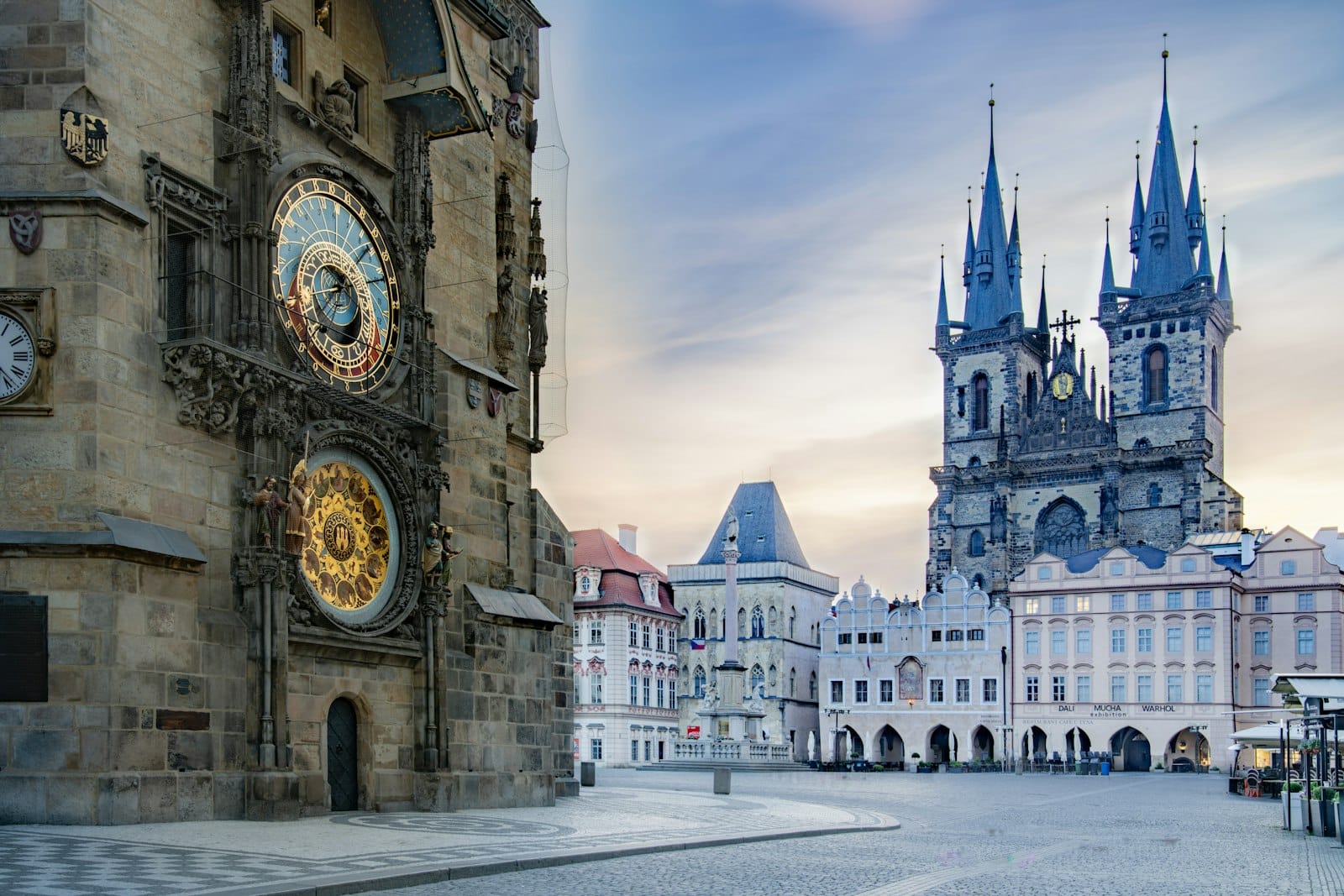 Der Altstädter Ring in Prag bei Sonnenaufgang mit der Astronomischen Uhr und der Týnkirche mit leeren Kopfsteinpflasterstraßen.