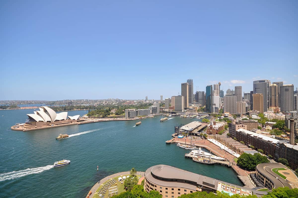 Weite, sonnige Luftaufnahme des Sydney Harbour mit der Opera House, den Kais am Circular Quay, Fähren, The Rocks und der Skyline der Innenstadt.