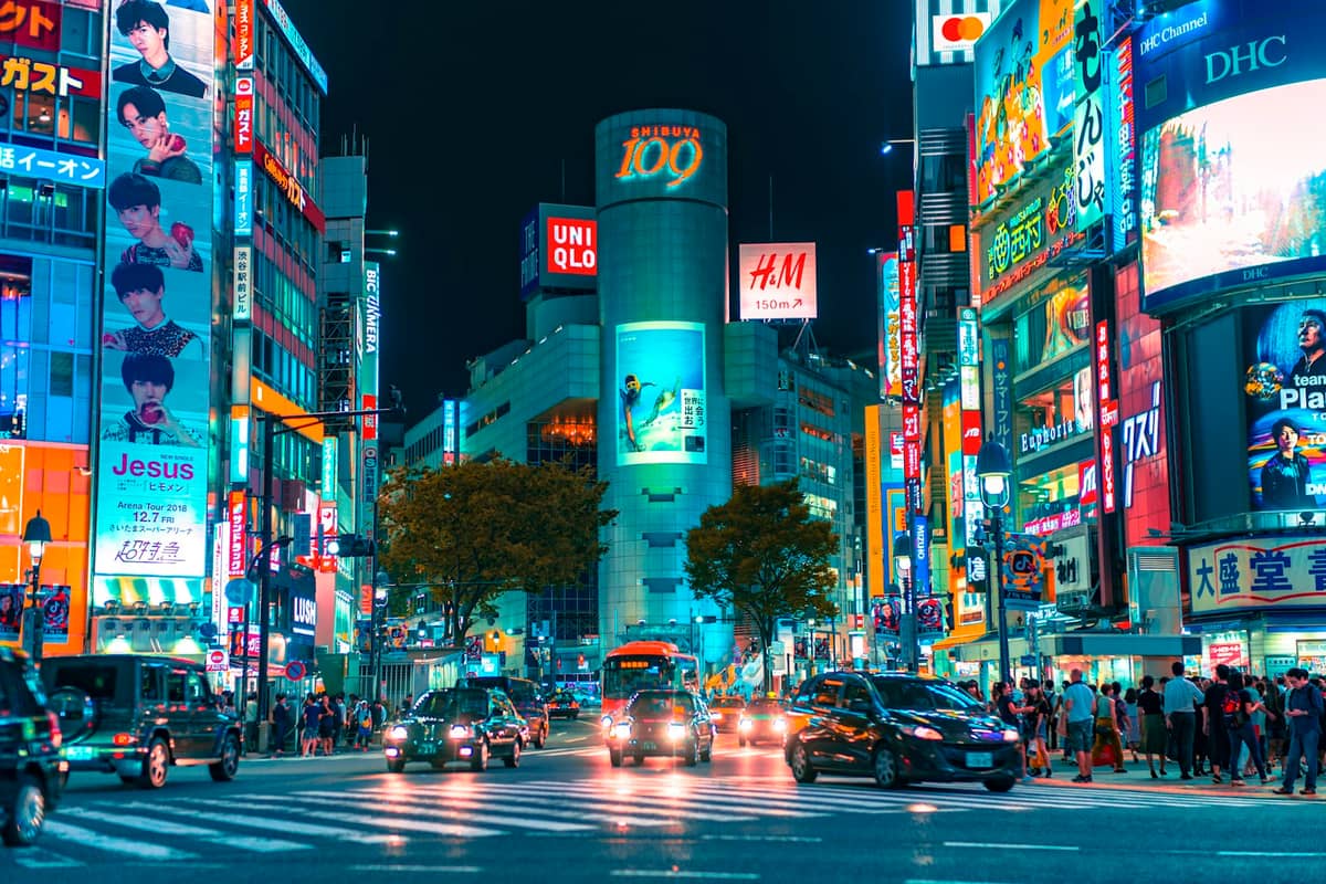 Shibuya Crossing at night in Tokyo, with crowds, neon signs, and the distinctive '109' building on a busy city street.