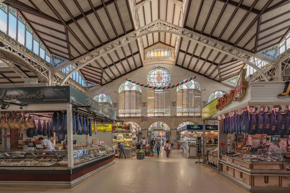 Weitwinkelansicht des Innenraums des Mercado Central de Valencia mit Jugendstilarchitektur, Buntglasfenstern und Marktständen mit lokalen Lebensmitteln.