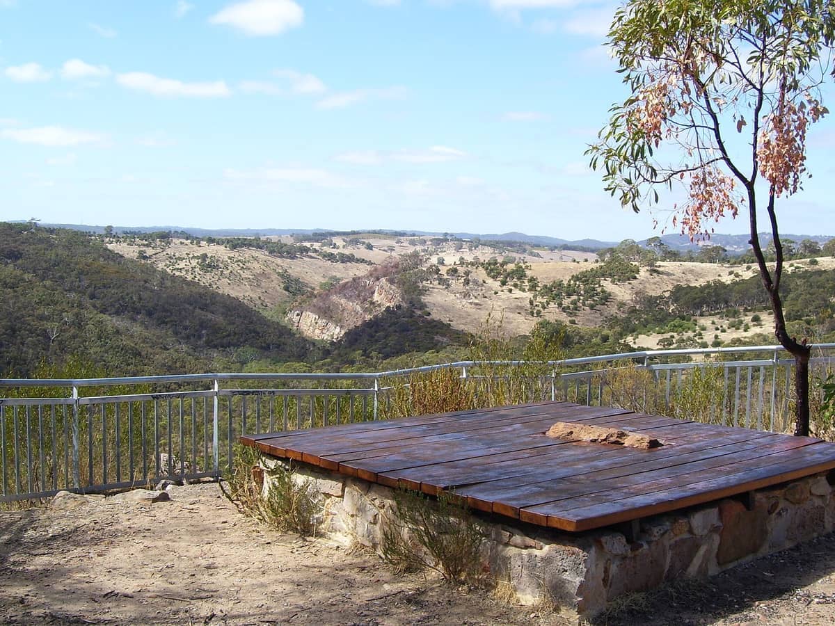 Scenic lookout point at Onkaparinga River National Park, featuring wooden platform, metal railing, distant gorge, and rolling hills under a bright sky.