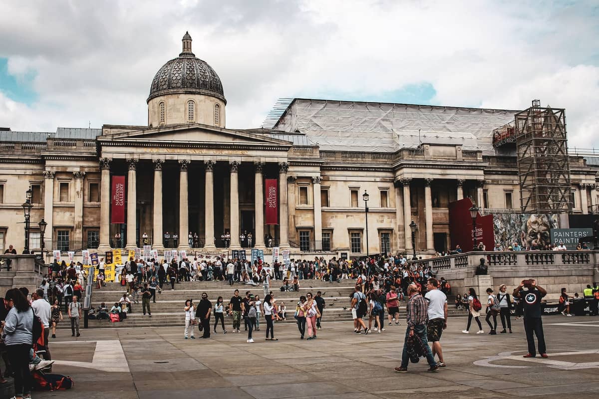 Multidões de pessoas se reúnem em frente à National Gallery em Trafalgar Square, Londres, em um dia ensolarado.