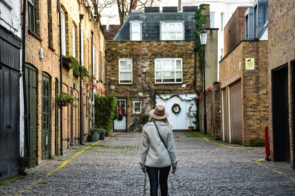 Pessoa caminhando por uma pitoresca rua mews de Londres com casas de tijolo, paralelepípedos e caráter residencial, sugerindo um ambiente de bairro.
