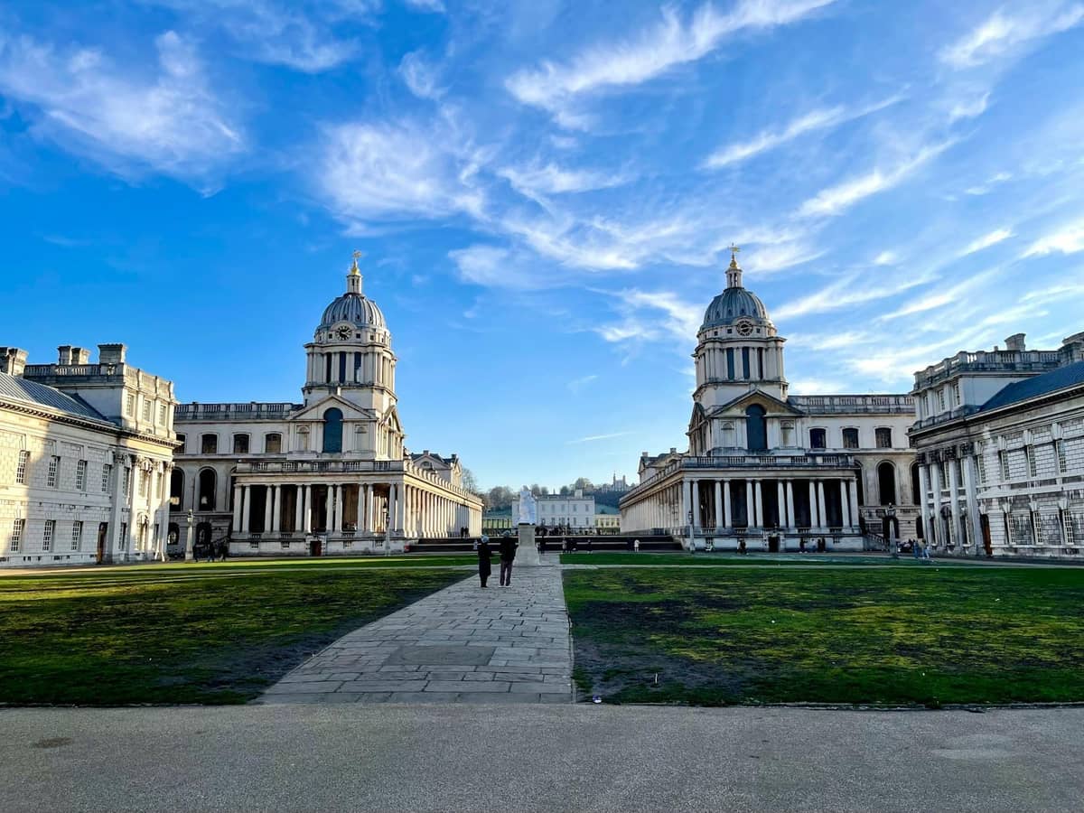 Vista ampla dos históricos edifícios com cúpulas e colunatas do Old Royal Naval College em Greenwich, Londres, sob um céu azul.