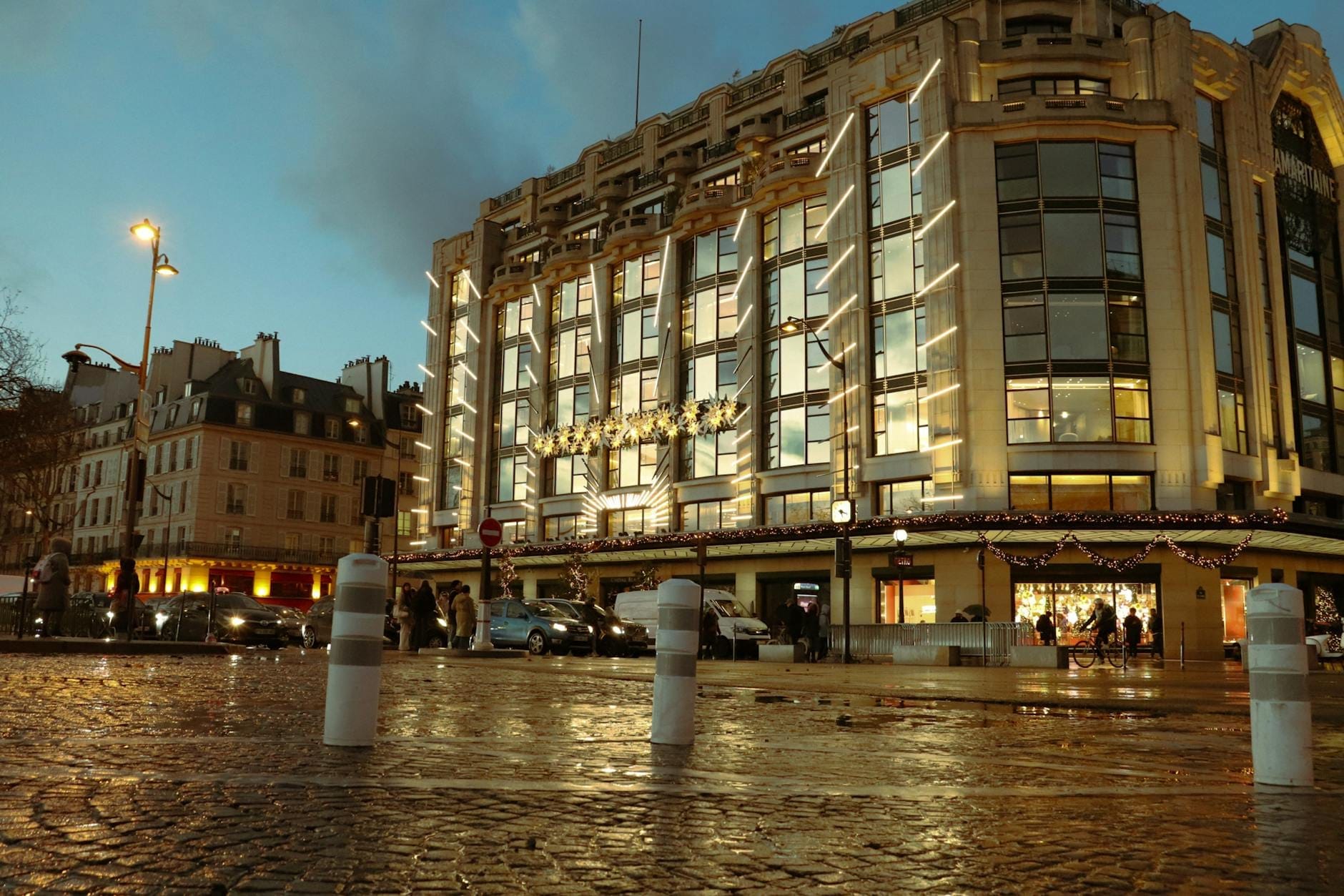 La facciata moderna in vetro e acciaio dell'Opéra Bastille illuminata al crepuscolo, con persone e auto in Place de la Bastille, Parigi.
